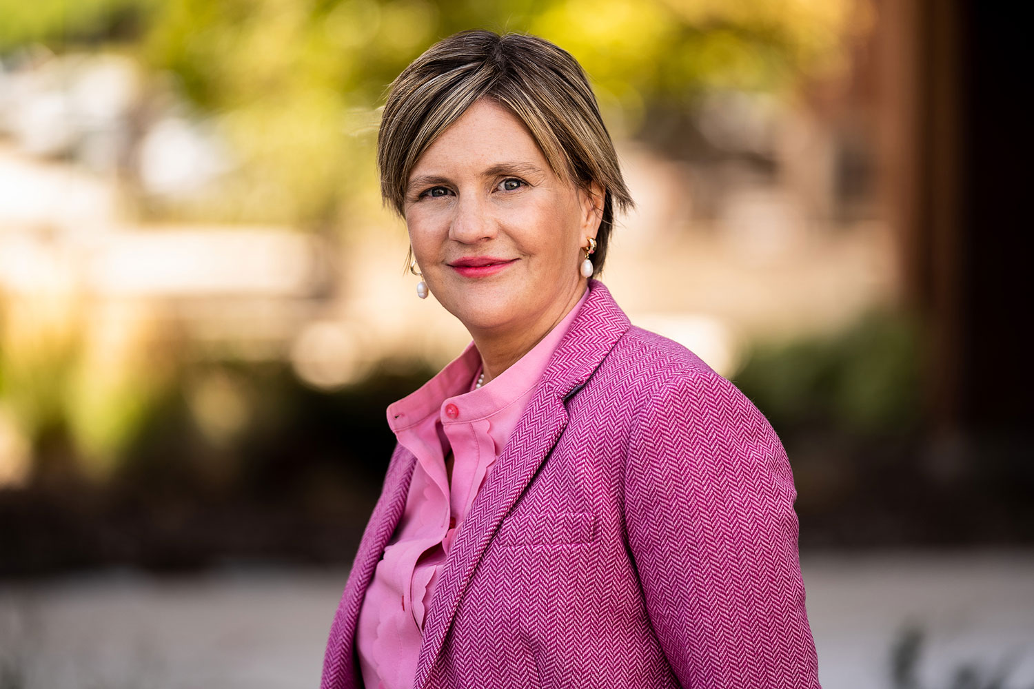 A headshot of a middle aged white woman smiling wearing a pink blazer and blouse