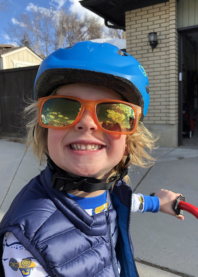 a little kid wearing sun glasses and a bike helment, smiling at the camera
