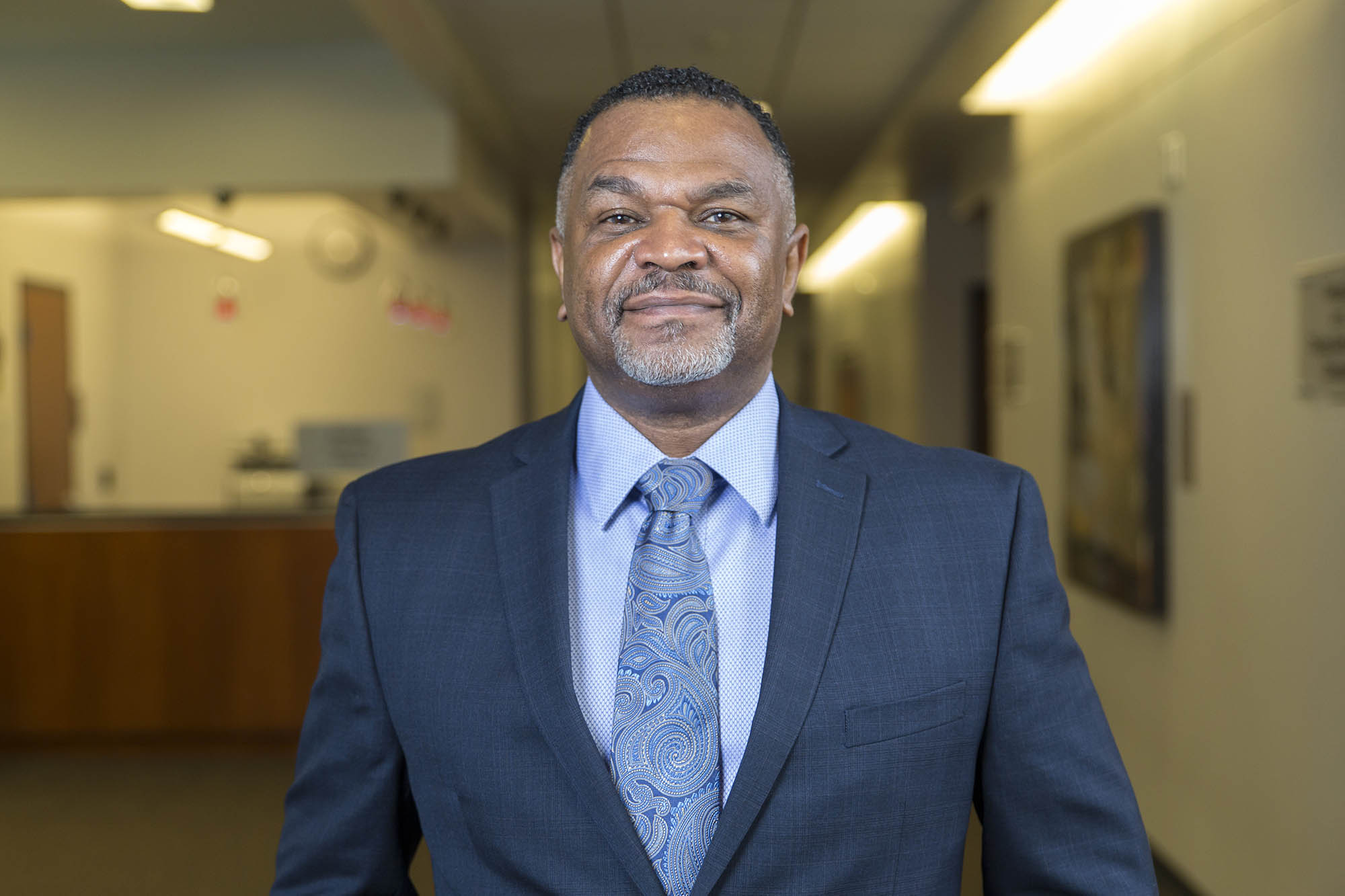 Dean Martell Teasley smiles at the camera, standing in the hallway of the Goodwill Humanitarian Building
