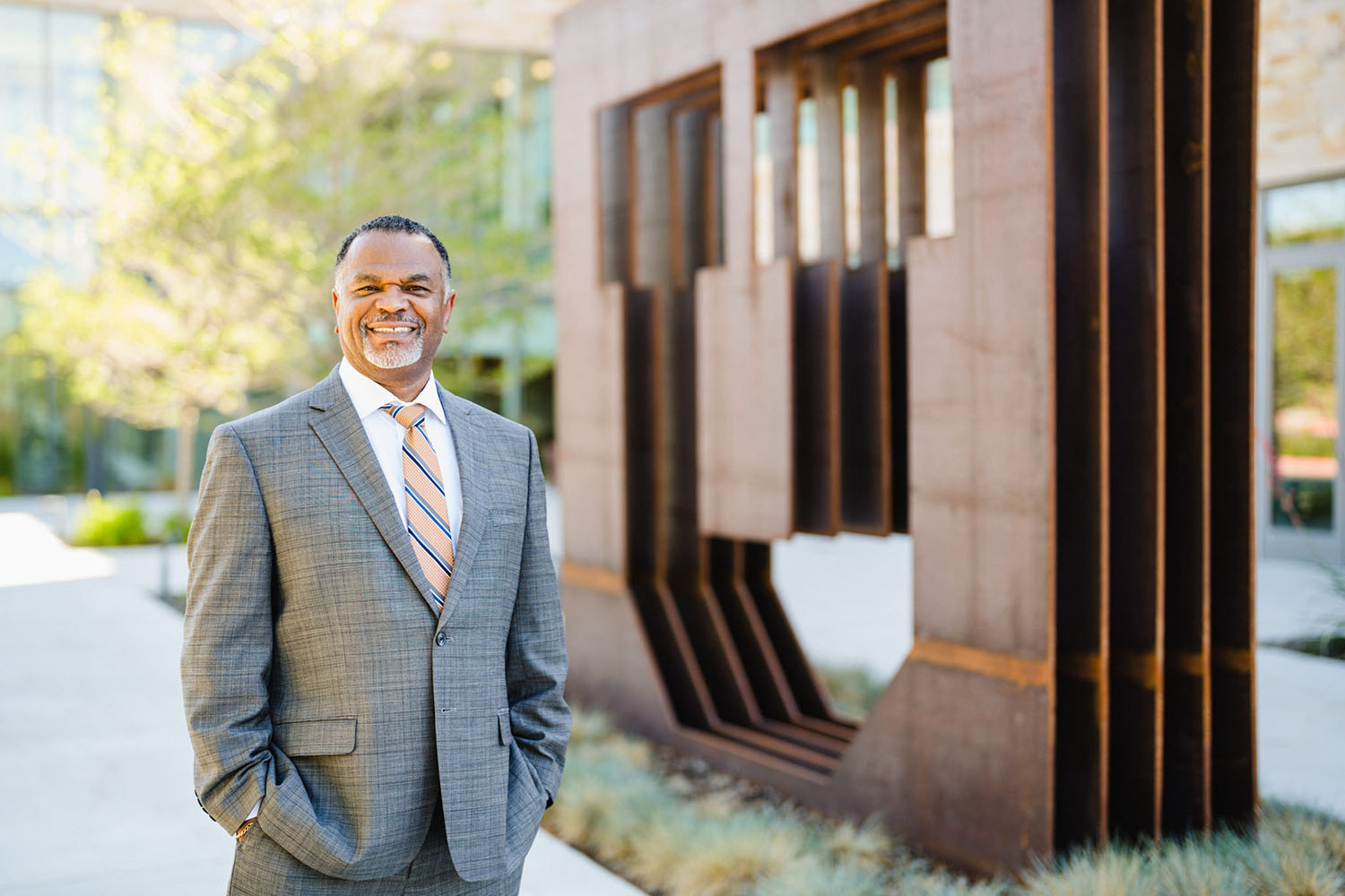 Photo of Martell Teasley, smiling and looking at the camera, standing next to a larg copper block U