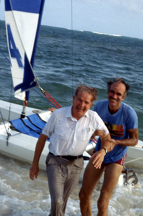 Two laughing men in wet clothing walk away from a boat.