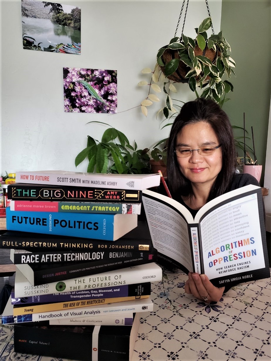 Dr. Jaeehee Yi reading with a stack of books next to her