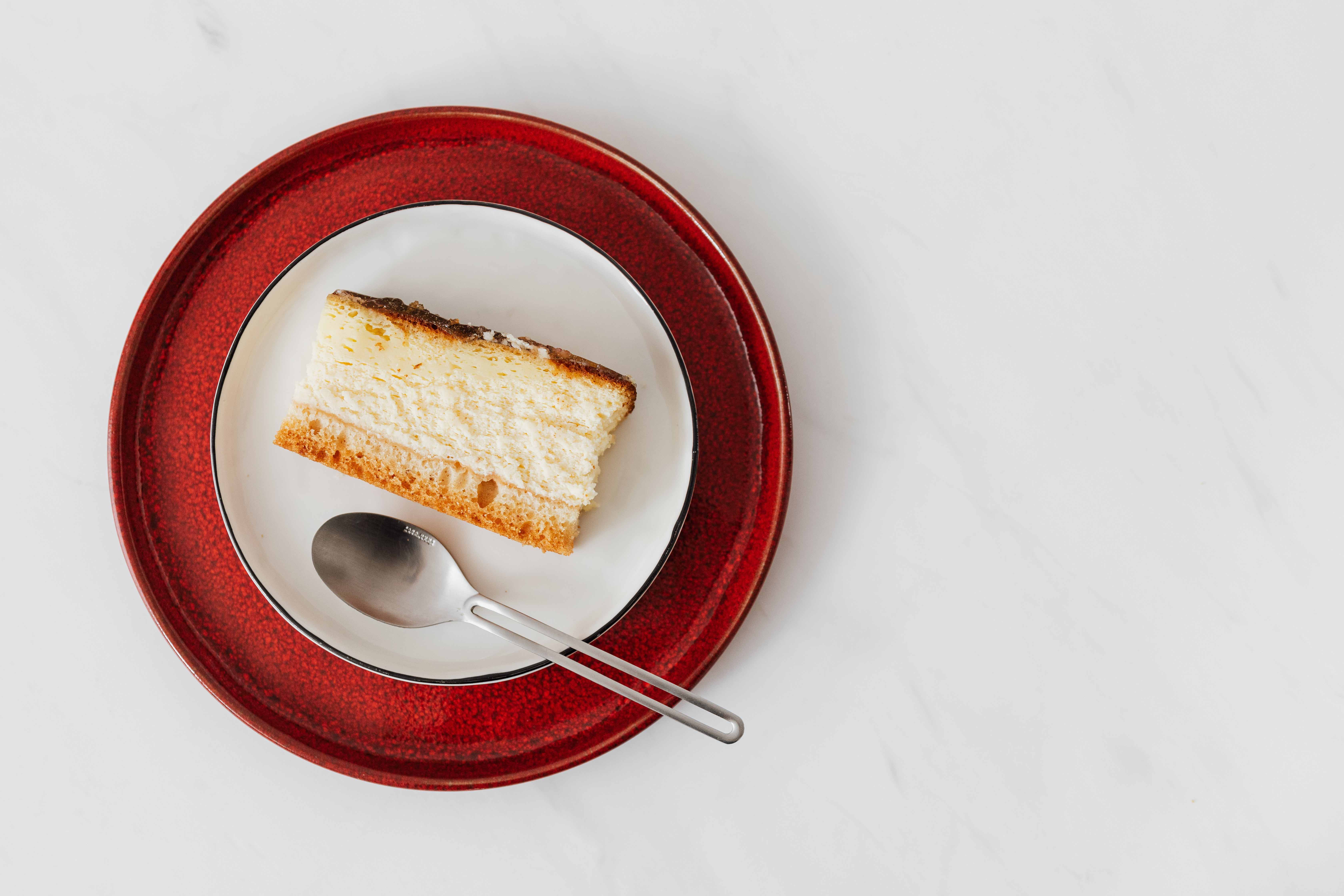 A plated piece of cake on a red plate with a spoon next to it.