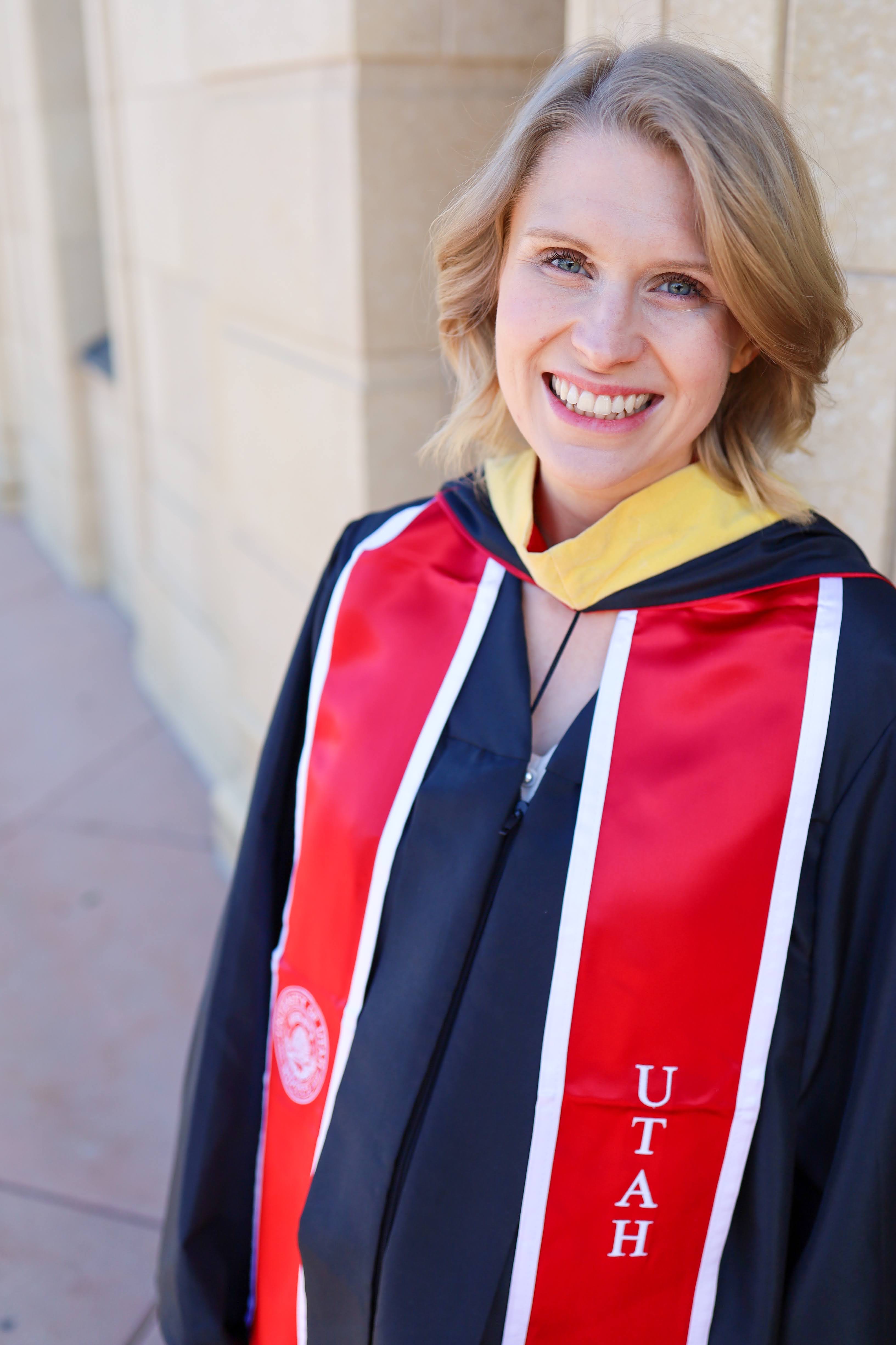 A headshot photo of a smiling young woman in graduation regalia outside.