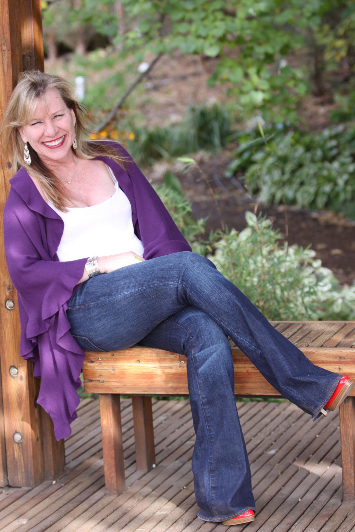 a white woman sits on a bench with her legs crossed and smiling
