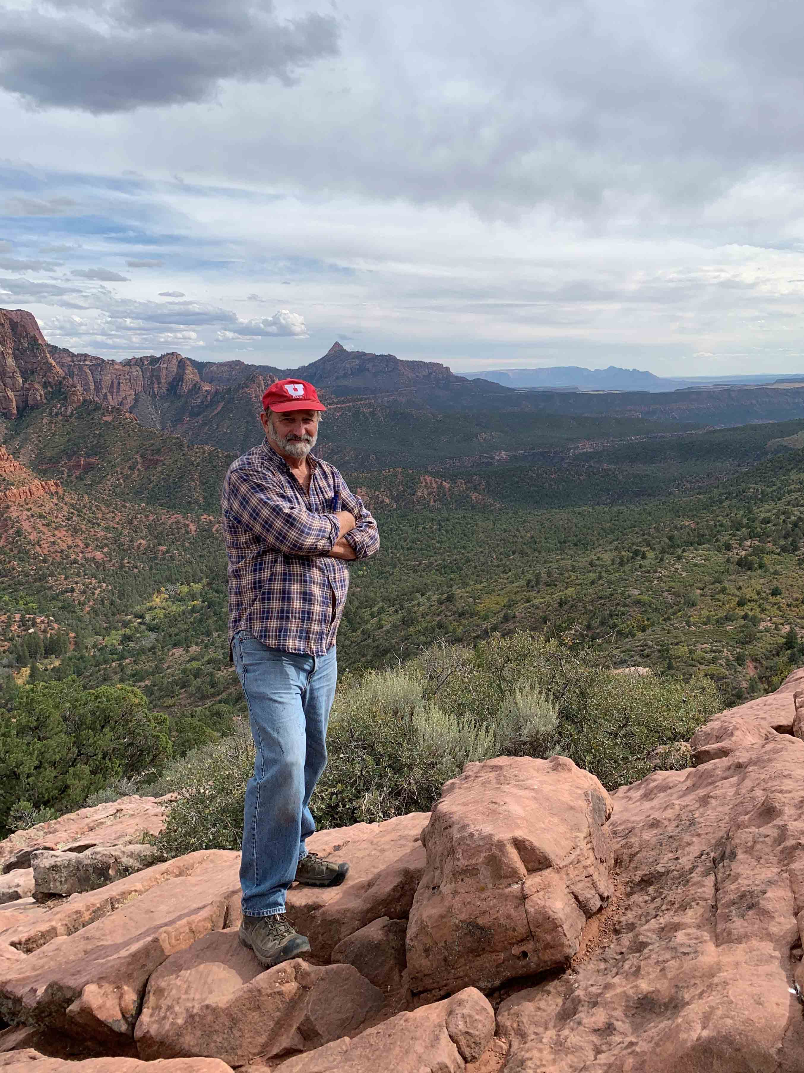 a man in a baseball cap stands in an outdoor setting with mountains rising in the background