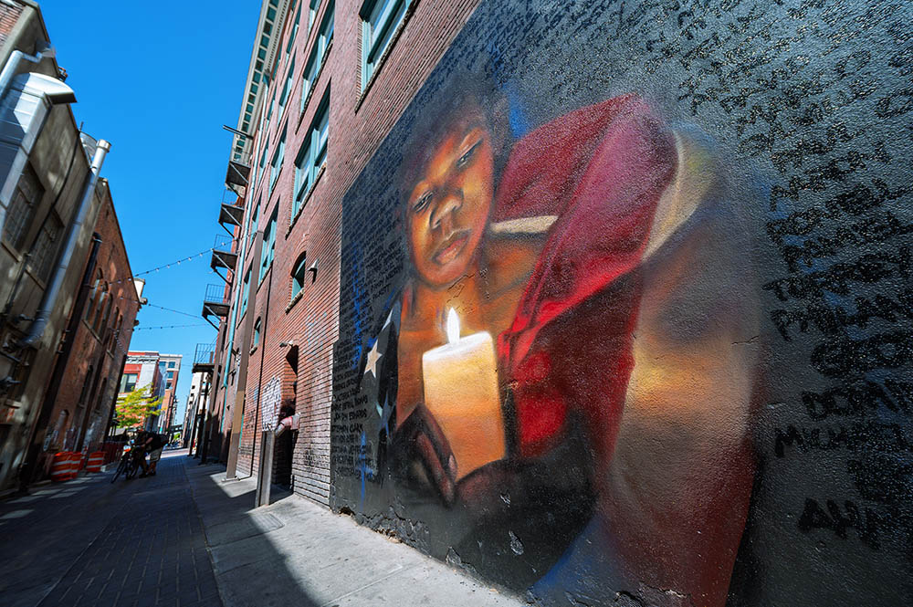 Photo of a mural (painted on the side of a building) depicting a pensive Black person wrapped in a U.S. flag and holding a lit candle.