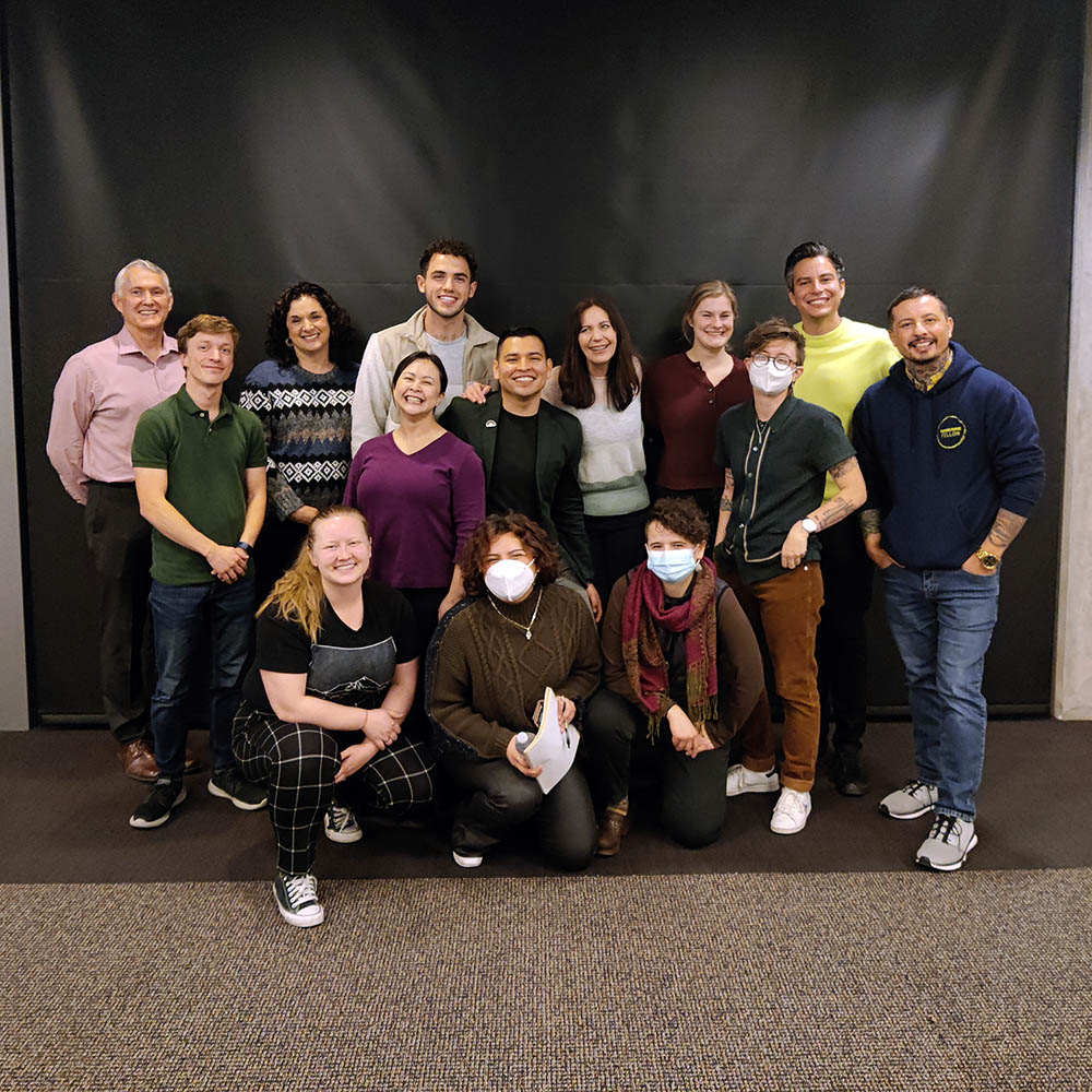 A group of about 15 people stand and crouch in a group, looking at the camera