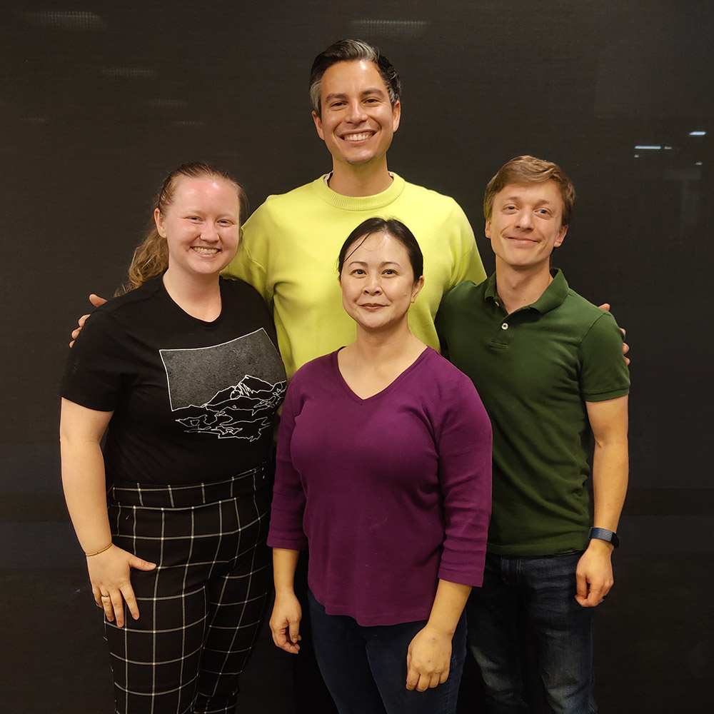 A group of four students stand together and look at the camera