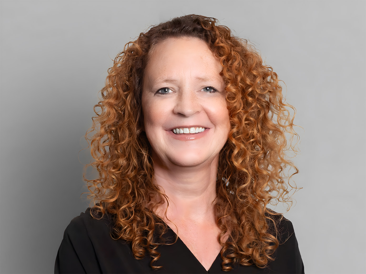 A smiling woman wearing black up against a plain backdrop.