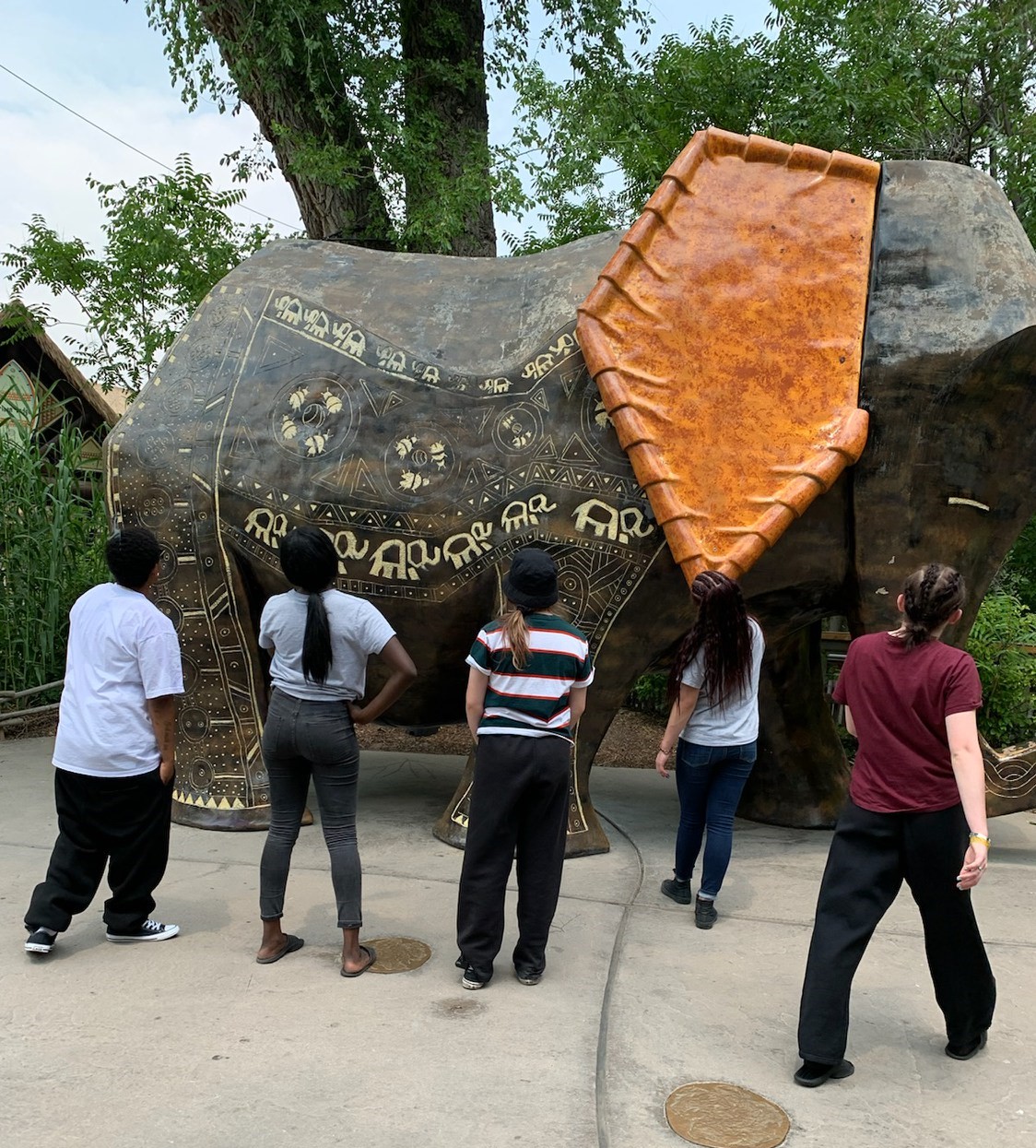 the backs of a group of kids in front of a large outdoor statue of an elephant