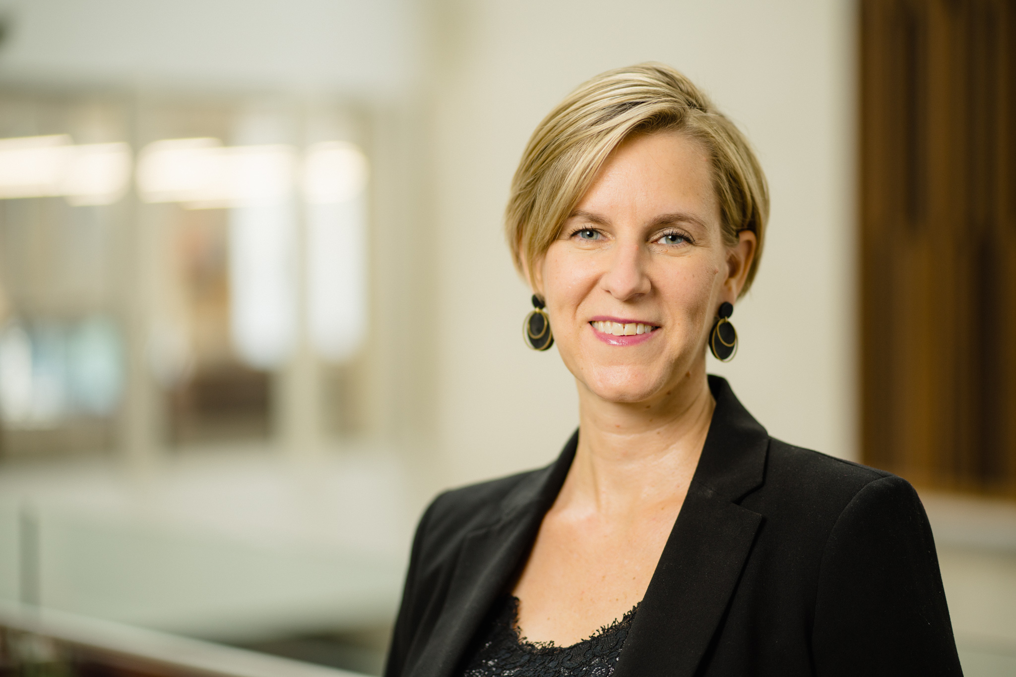 A headshot of a white woman smiling with architectural details in the background