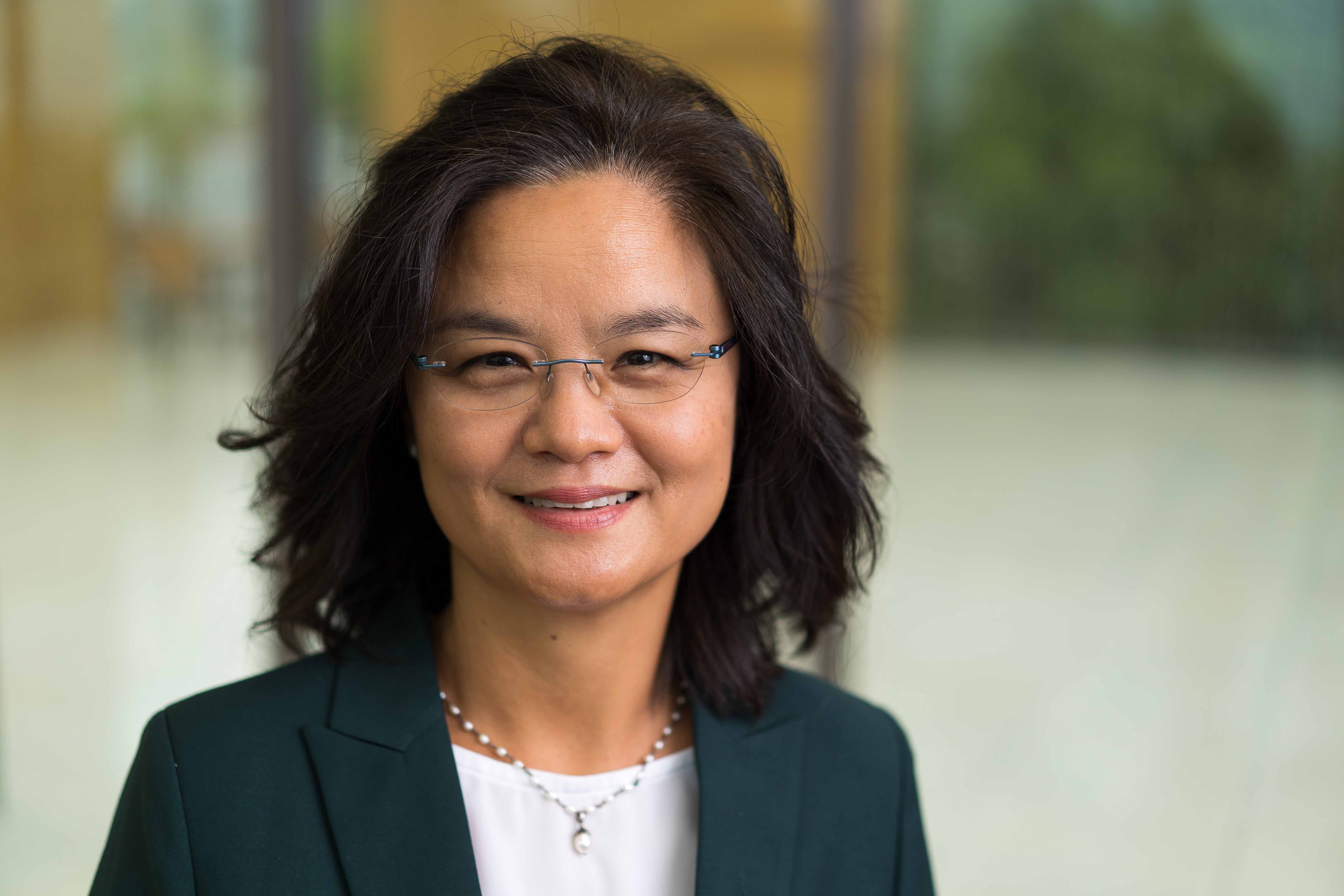 A photo of Dr. Jaehee Yi - a middle aged Asian woman wearing glass with indoor architectural details in the background