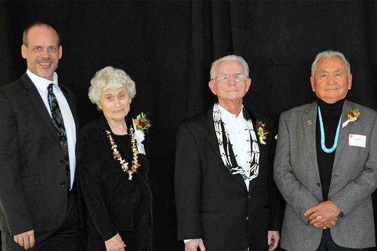 Four middle aged and older adults in semi formal clothing standing in front of a black curtain
