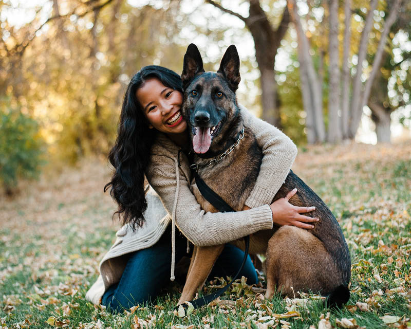 a young asian amerian woman hugs a dog in an autumn, outdoor landscape