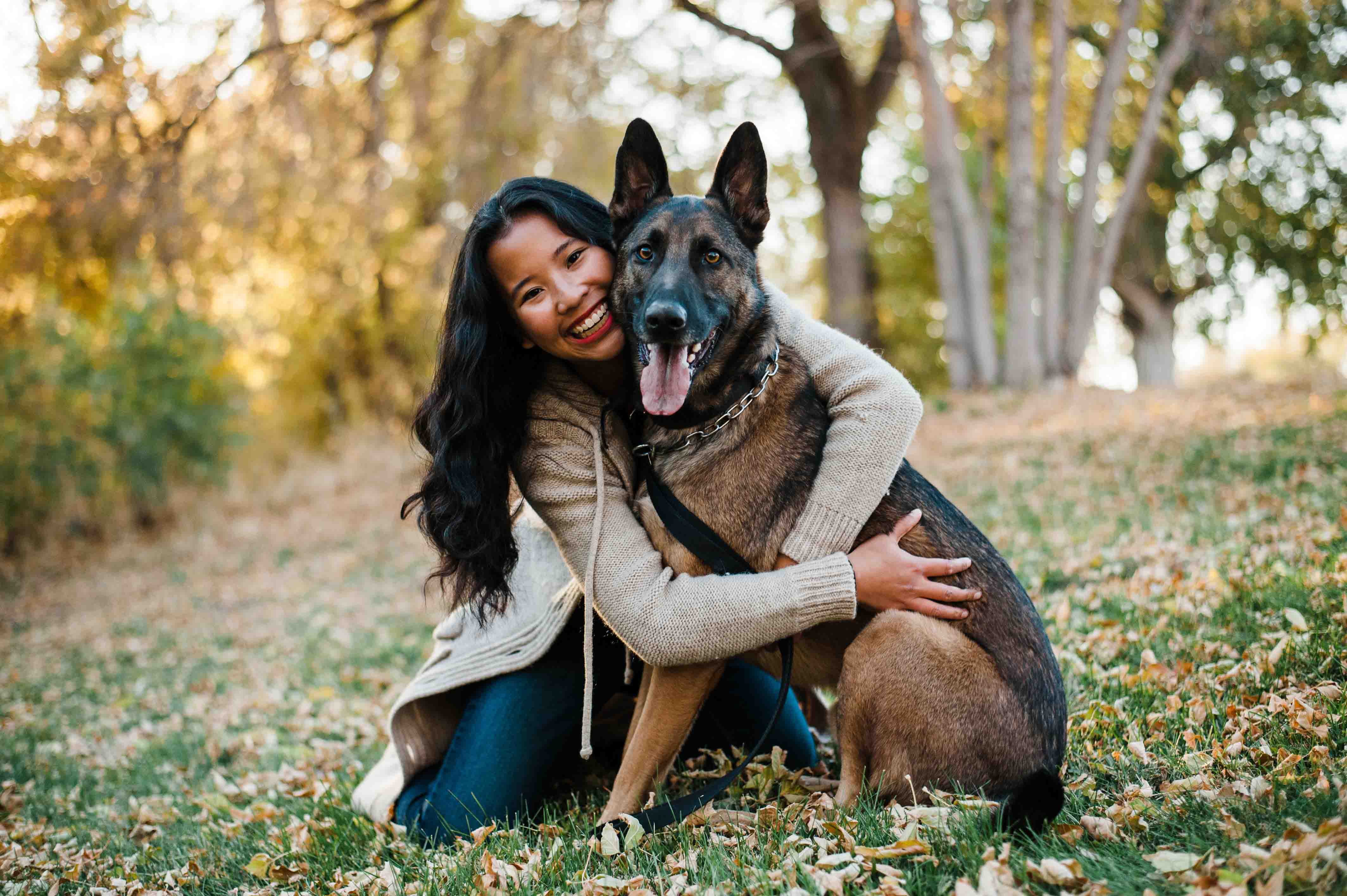 a young asian amerian woman hugs a dog in an autumn, outdoor landscape