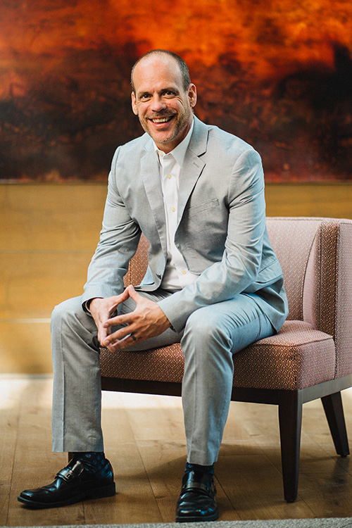 Photo of Dean Philip Osteen seated in front of a piece of artwork